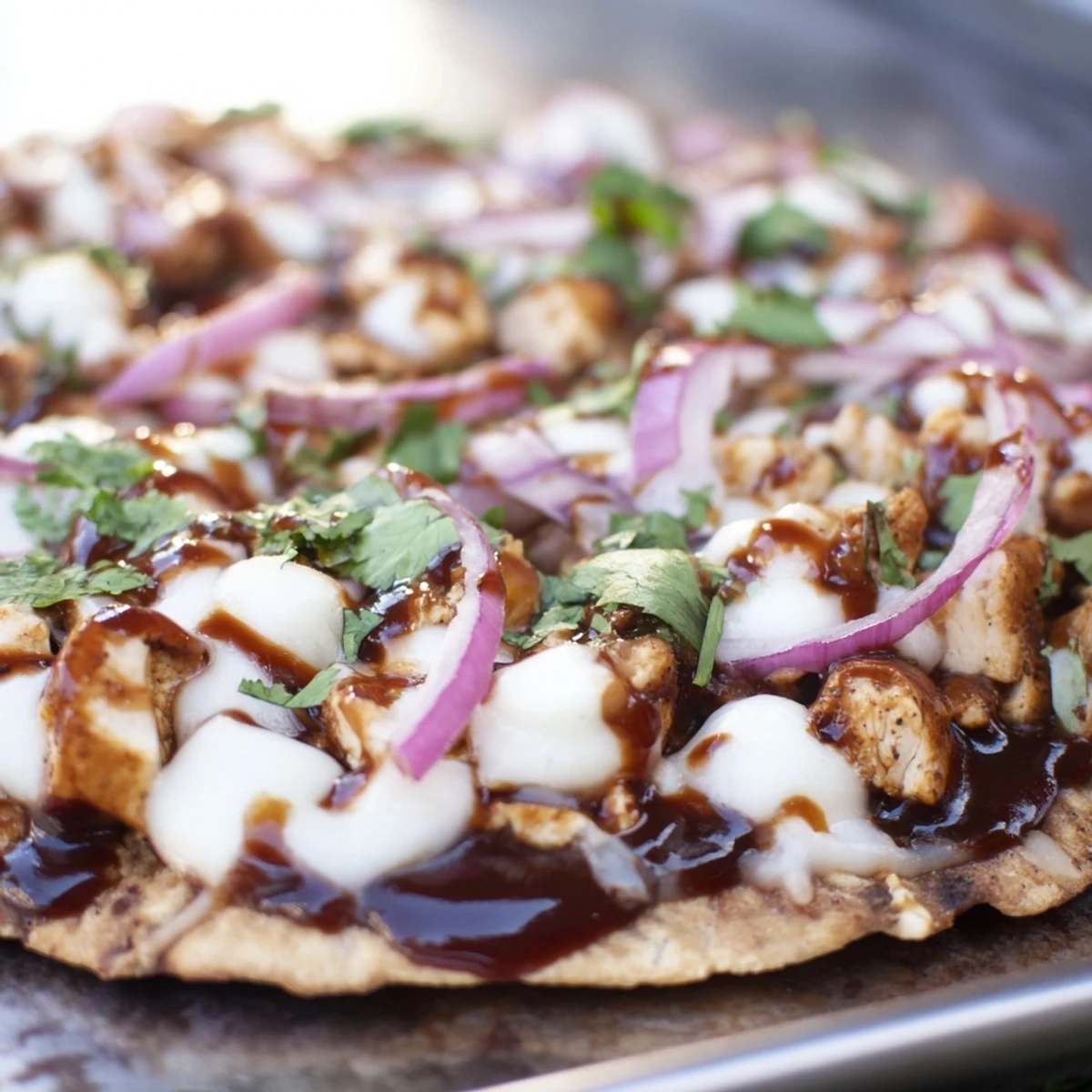 A close-up view of BBQ Chicken Flatbread fresh from the oven, featuring melted mozzarella, tender grilled chicken, and red onion on a crispy crust.  