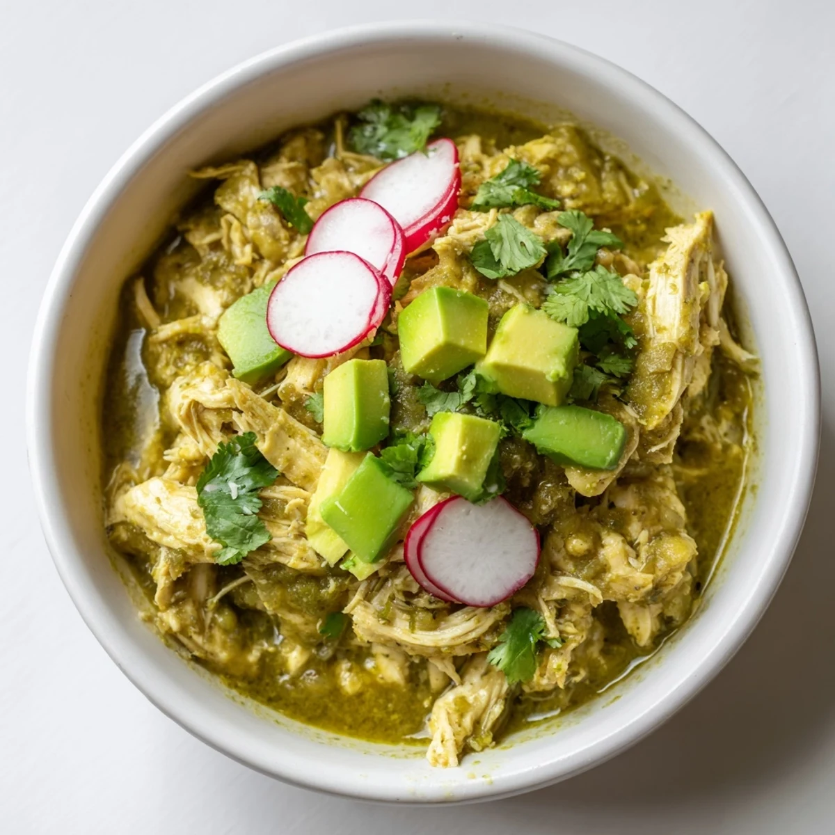 Steaming Chicken Chili Verde with shredded chicken in a vibrant green tomatillo sauce, topped with avocado and cilantro for a zesty meal.