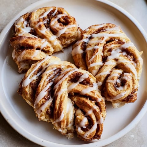 Flaky, golden air-fryer cinnamon roll twists, warm from the air fryer, drizzled with sweet glaze.