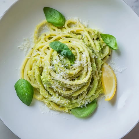 Vibrant creamy avocado pasta coated in a luscious green sauce, garnished with fresh basil.