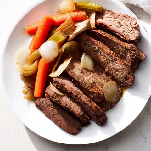 A close-up of slow-cooked classic brisket, juicy with vegetables, resting next to a sweet potato mound.
