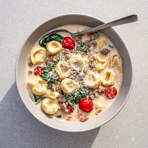 A steaming bowl of Tortellini Beef Soup, filled with tender cheese tortellini, savory ground beef, and halved cherry tomatoes in a creamy broth.